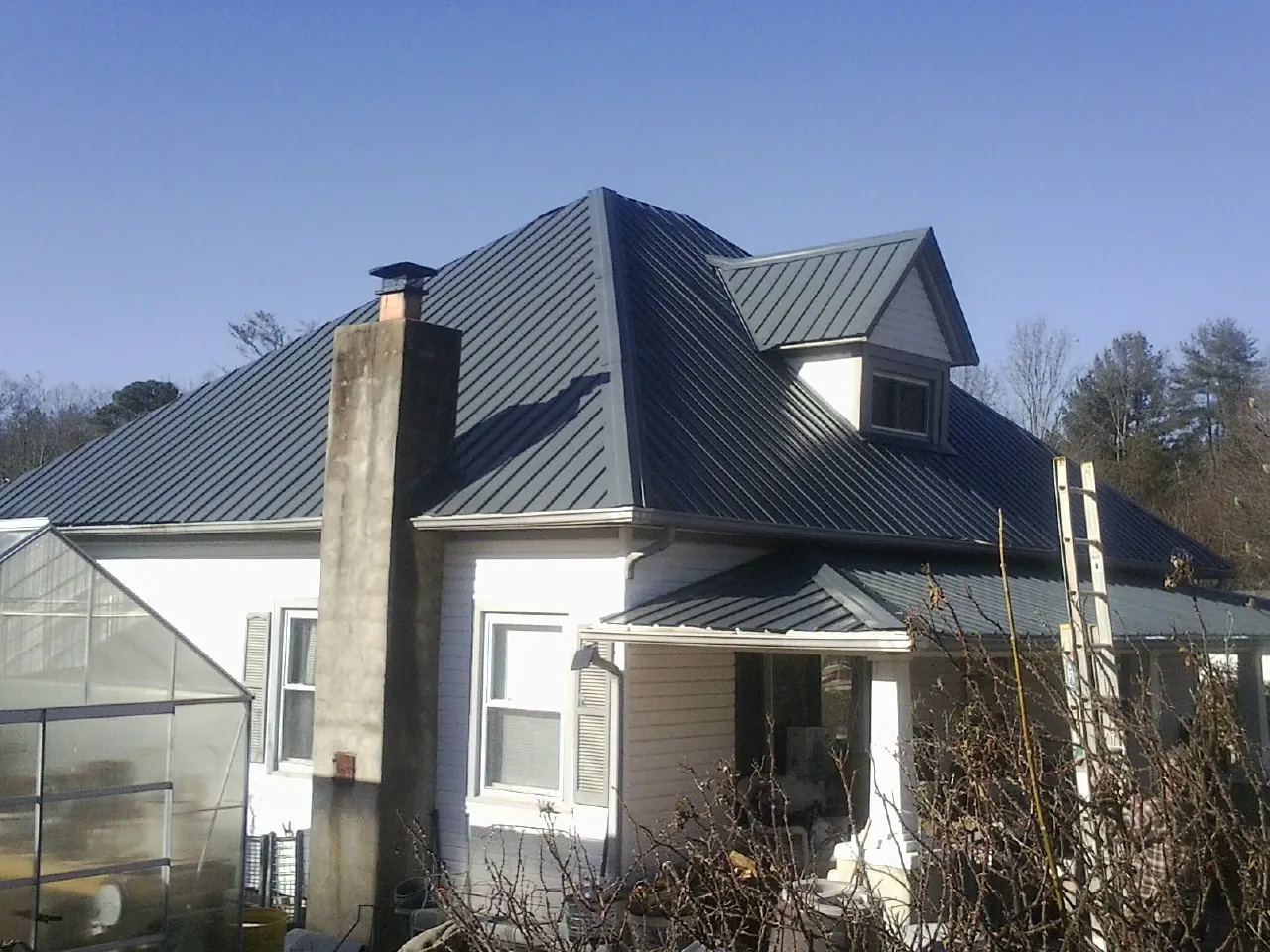 Dark blue standing seam metal roof on a white farmhouse with dormer — Slate & Tile Roof Repair by Roofing Brothers in Grey Eagle