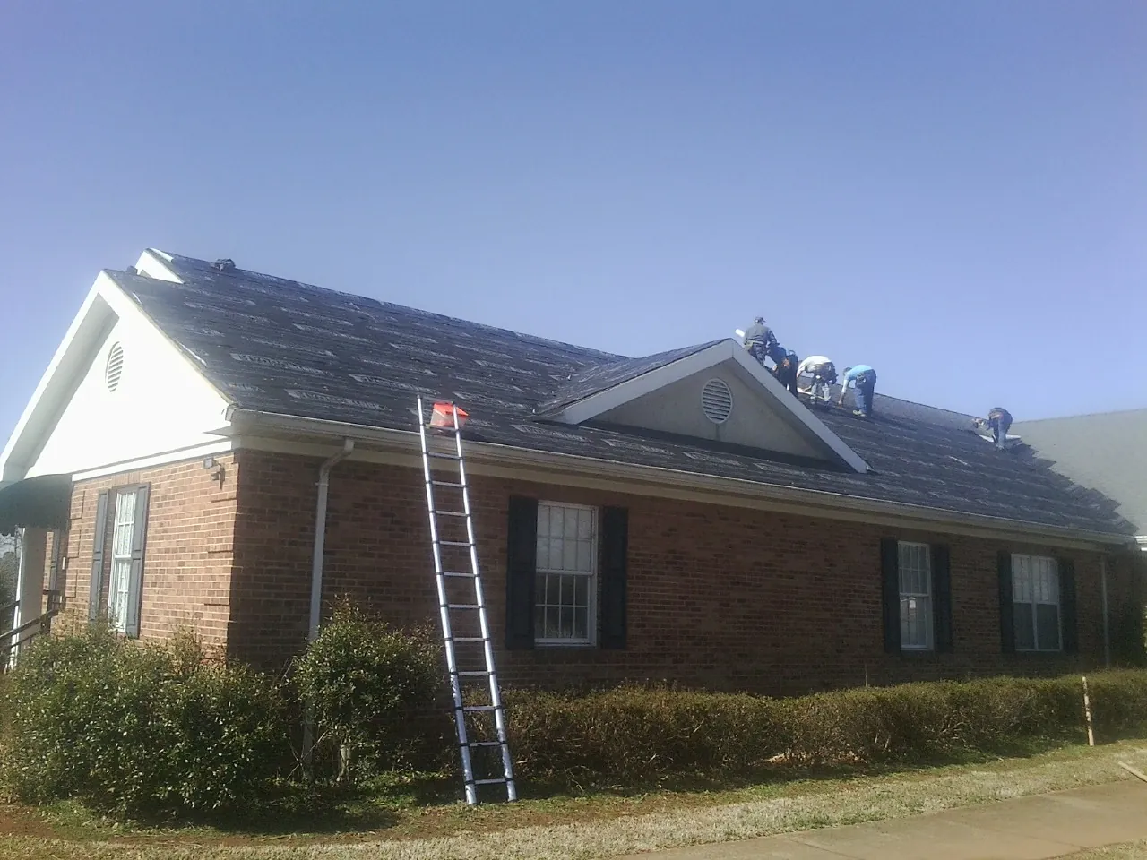Crew tearing shingles off a brick ranch roof with a ladder set — Metal Roof Repair work by our crew in Grey Eagle