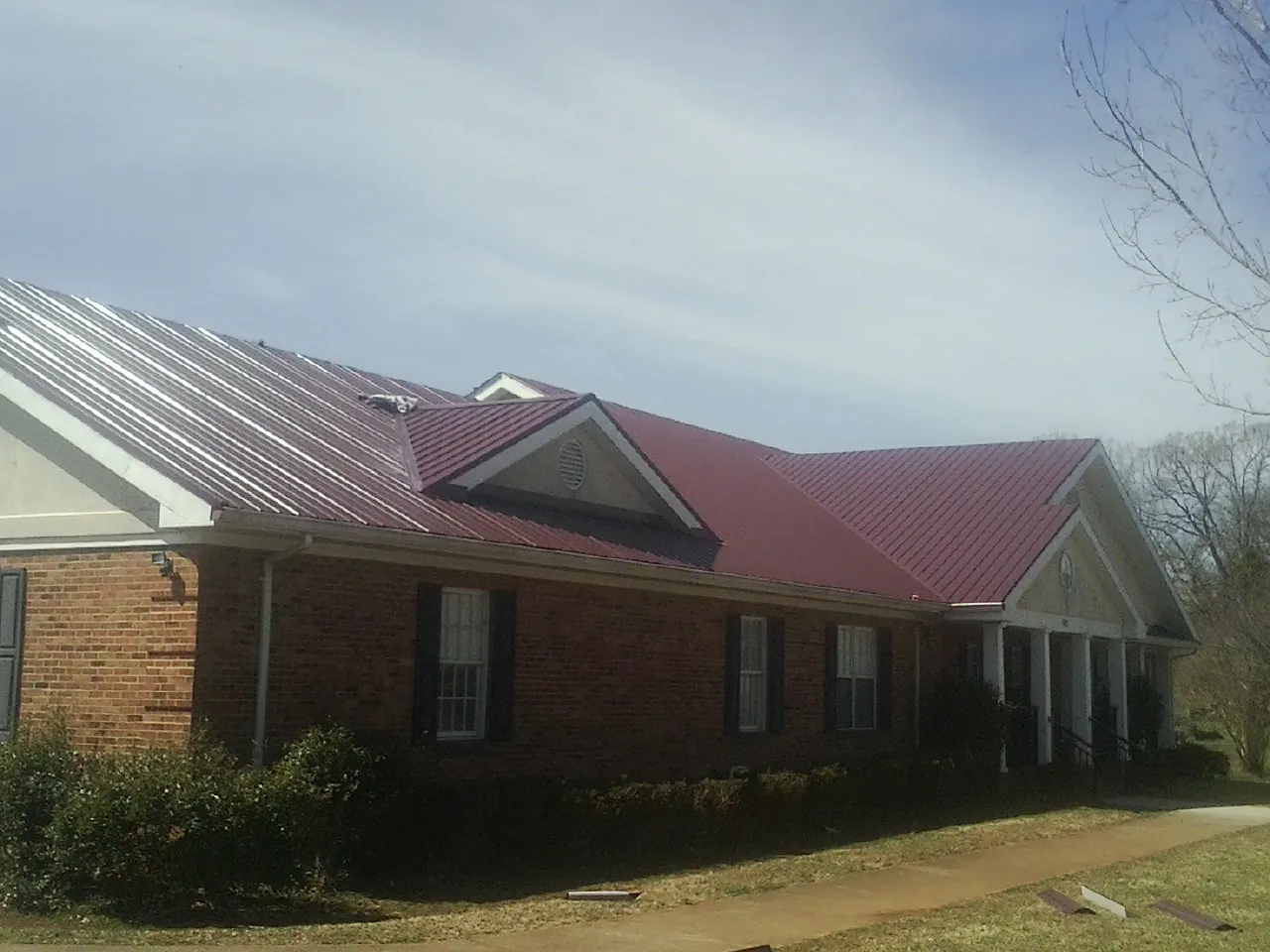 Red metal roof with gabled entries on a long brick building, from a Hail Damage Roof Repair job in Grey Eagle