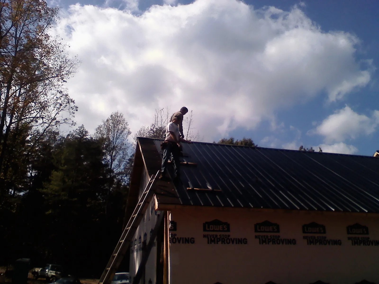 Roofer fastening dark metal panels high against a cloudy sky, from a Roof Inspection job in Grey Eagle
