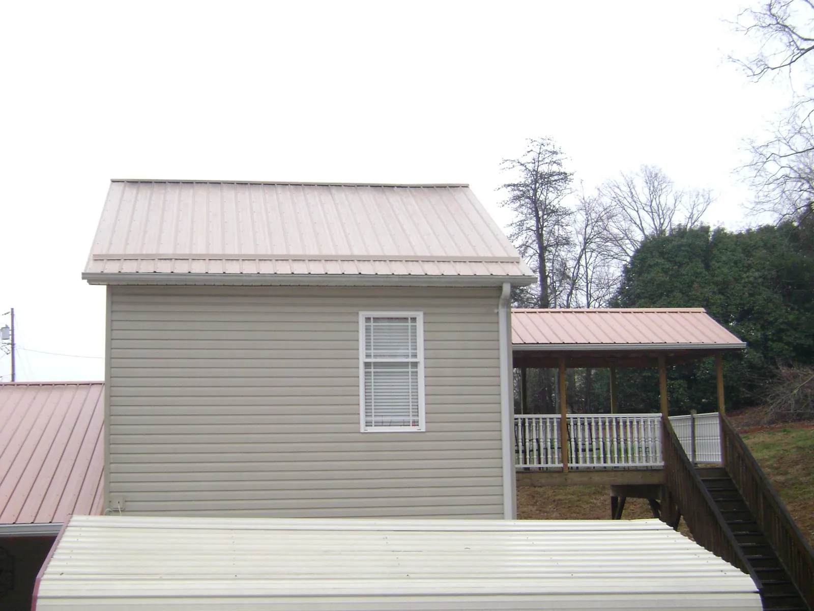 Tan metal roofs on a two story addition and attached porch, from a Roof Replacement job in Grey Eagle